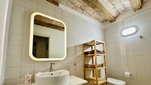 Une salle de bain avec un lavabo blanc, une étagère en bois, un miroir et des toilettes.