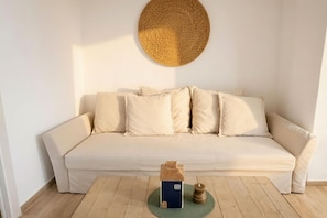 Ein sofa in neutralen Farben mit einem gewebten Wandbehang darüber und einem kleinen haussähnlichen Gegenstand auf dem Boden.