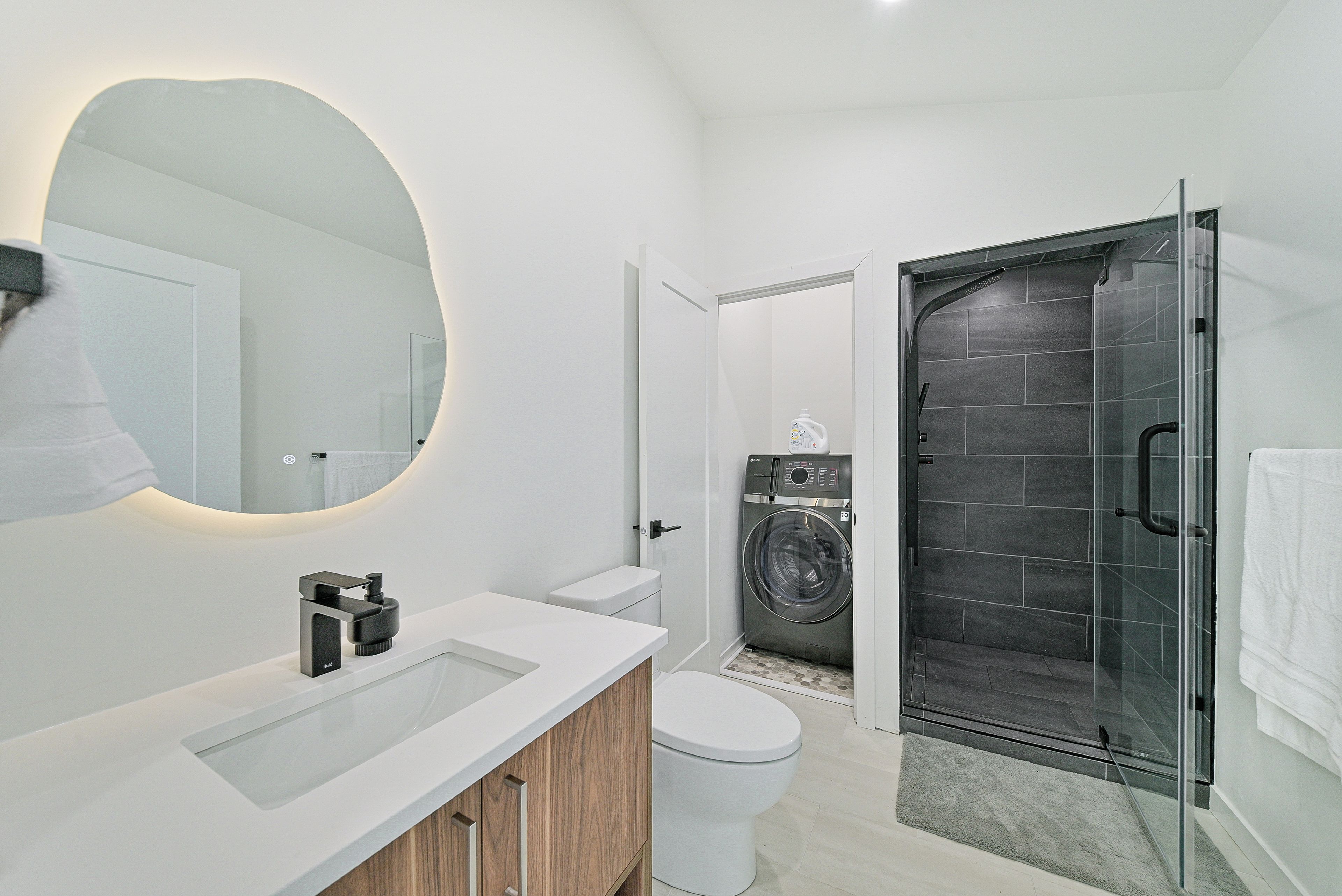 A modern bathroom with a glass shower enclosure, a built-in washing machine, and a large mirror.