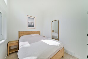 Un dormitorio con cama, mesita de noche, espejo y un cuadro en la pared.