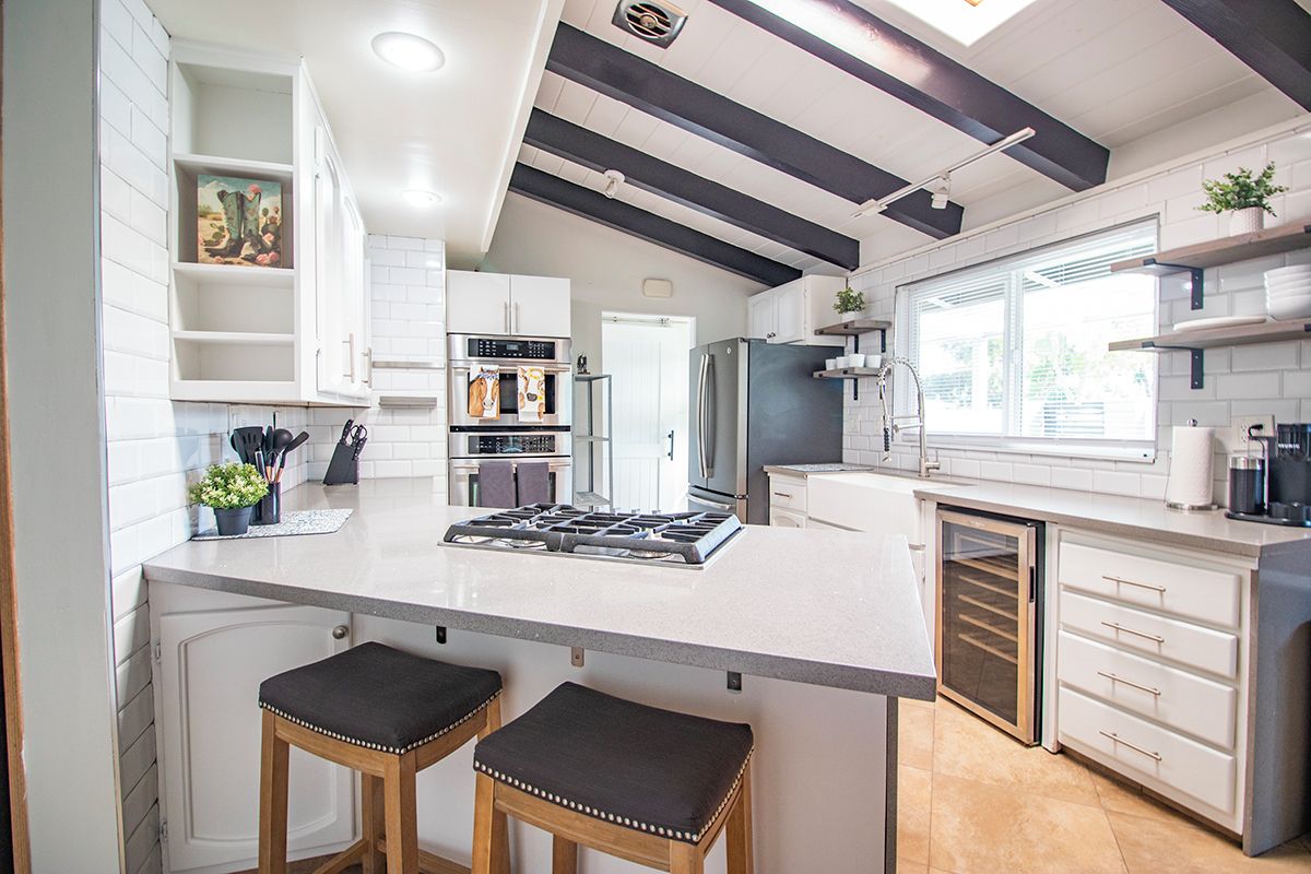 A modern kitchen with white cabinetry, a central island with stools, a built-in oven, and a refrigerator.