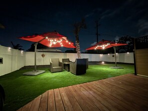 A backyard with artificial grass, wooden deck, outdoor furniture, and red umbrellas with lights. - Hot Tub-Pool Table-Near Beach and Wineries (Santa Maria)