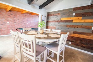 A dining area with a round table, white chairs, and a brick wall. - Hot Tub-Pool Table-Near Beach and Wineries (Santa Maria)