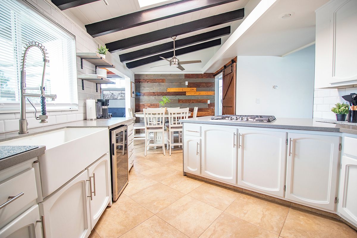 A modern kitchen with white cabinetry, a built-in stove, and a dining area with a wooden accent wall.