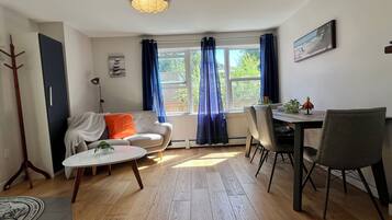A living room with a sofa, coffee table, dining table with chairs, a lamp, and a window with curtains.