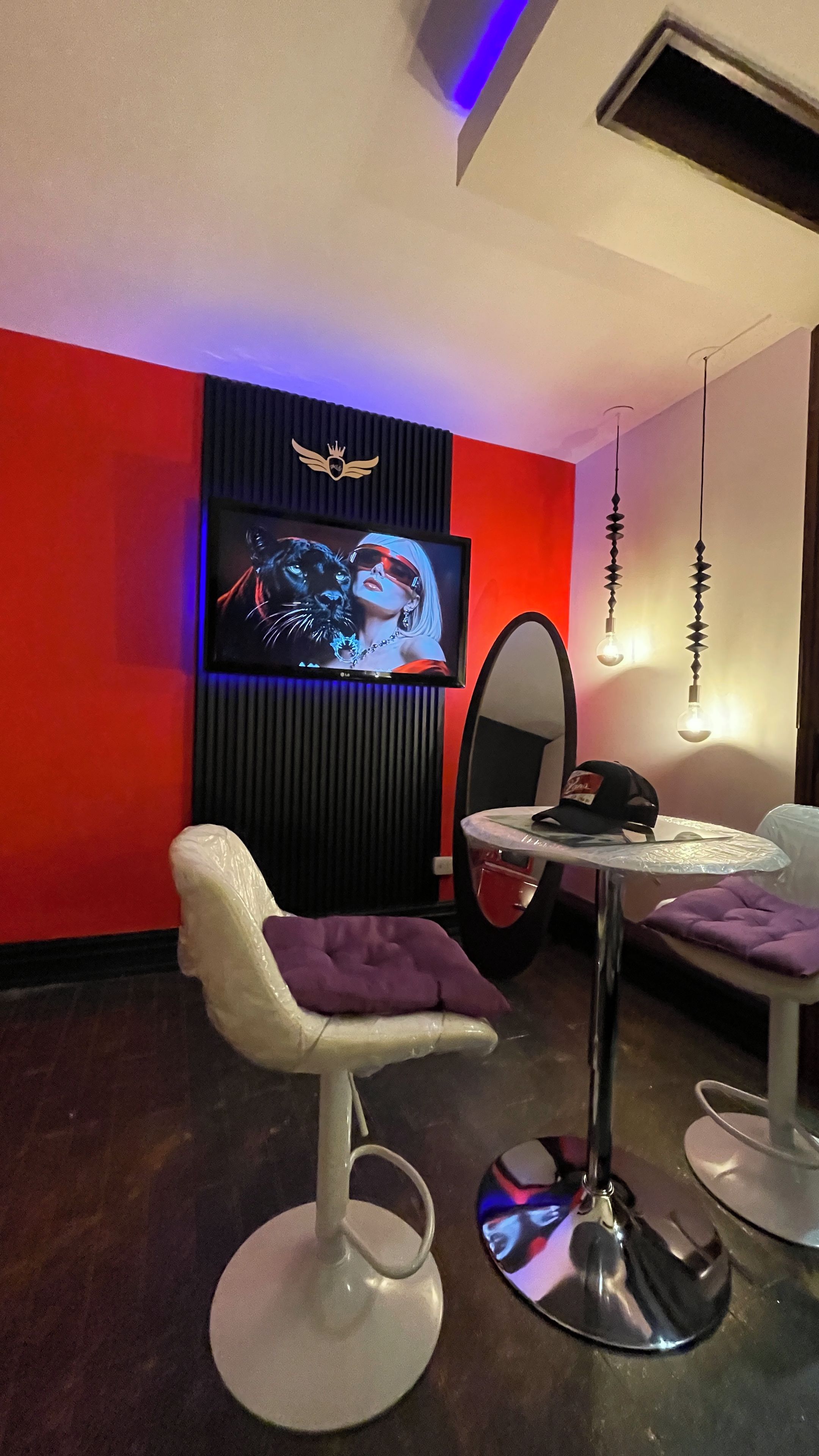 Ein modernes Zimmer mit einem an einer schwarzen Platte befestigten Fernseher, einem runden Spiegel und einem Tisch mit einem violetten Kissen.
