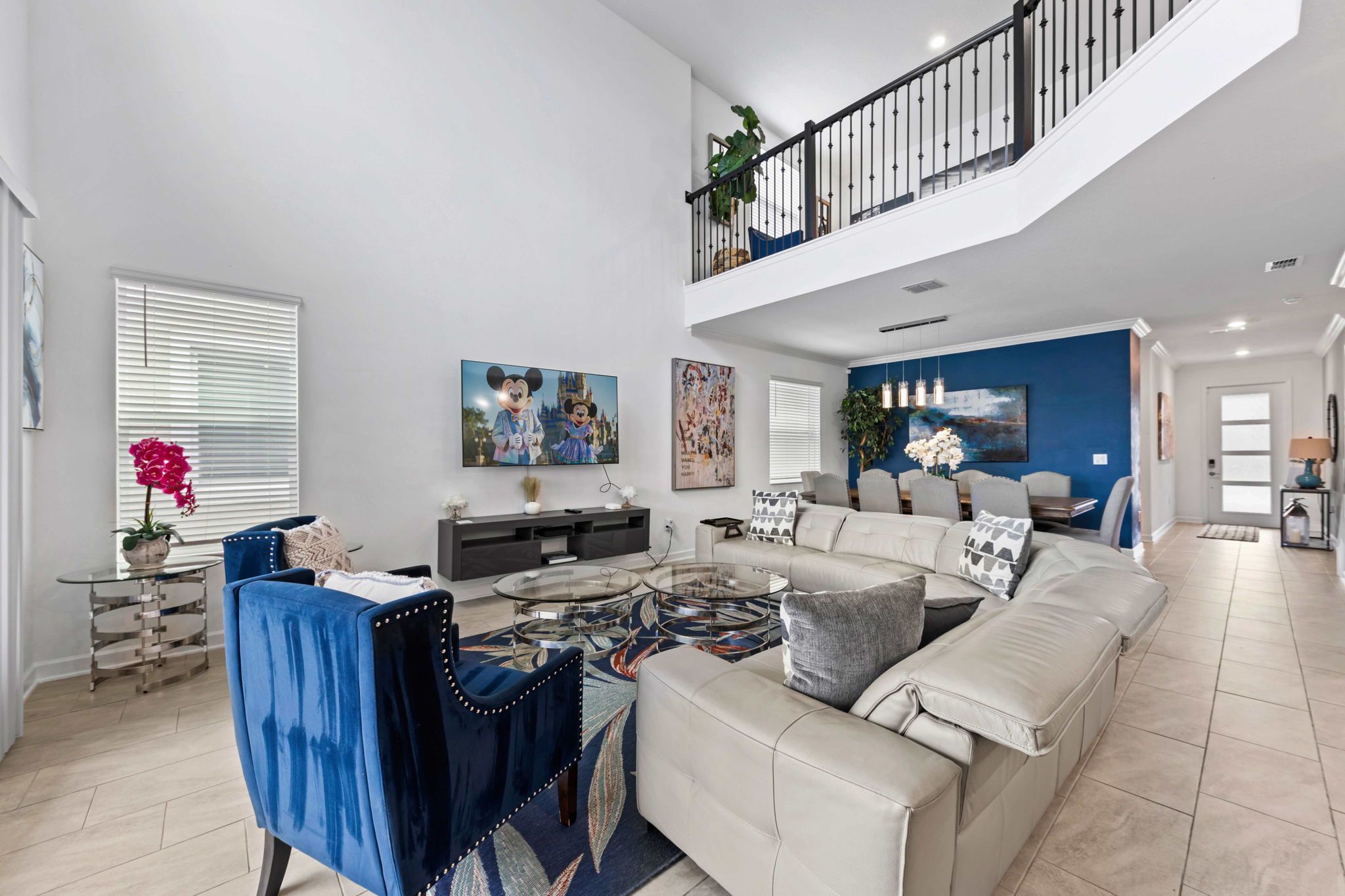 A spacious living room with a high ceiling, a sectional sofa, a coffee table, and a dining area with chairs.