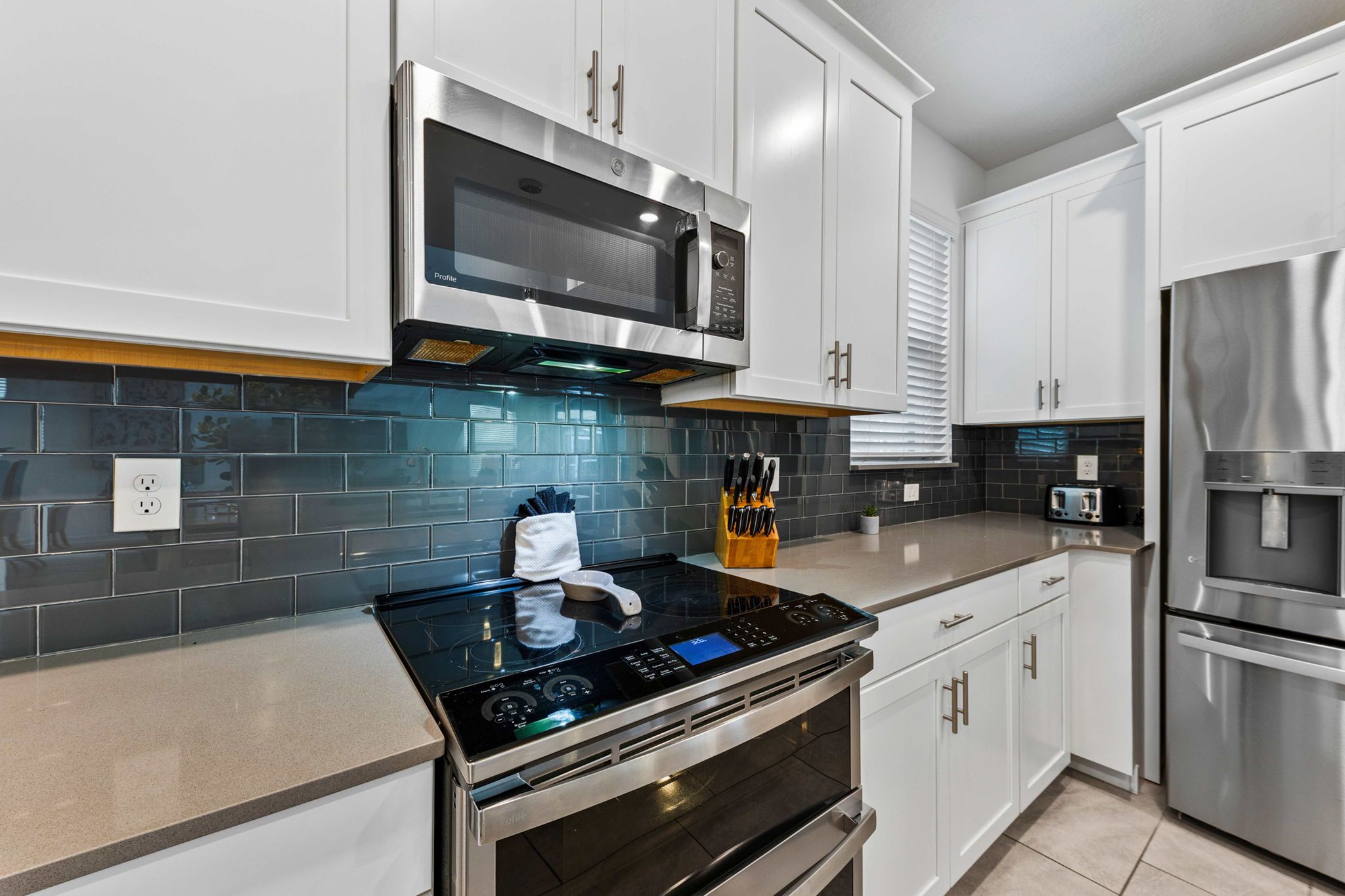 A modern kitchen with stainless steel appliances, a black induction cooktop, and white cabinetry.