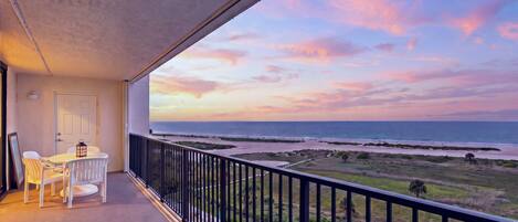 A balcony with a view of the ocean and beach at sunset.