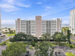 A multi-story hotel with a central tower, parking lot, and a view of the beach. - Beachfront Condo 2BR Gulf Views Monthly Stays Heated Pool (Clearwater)
