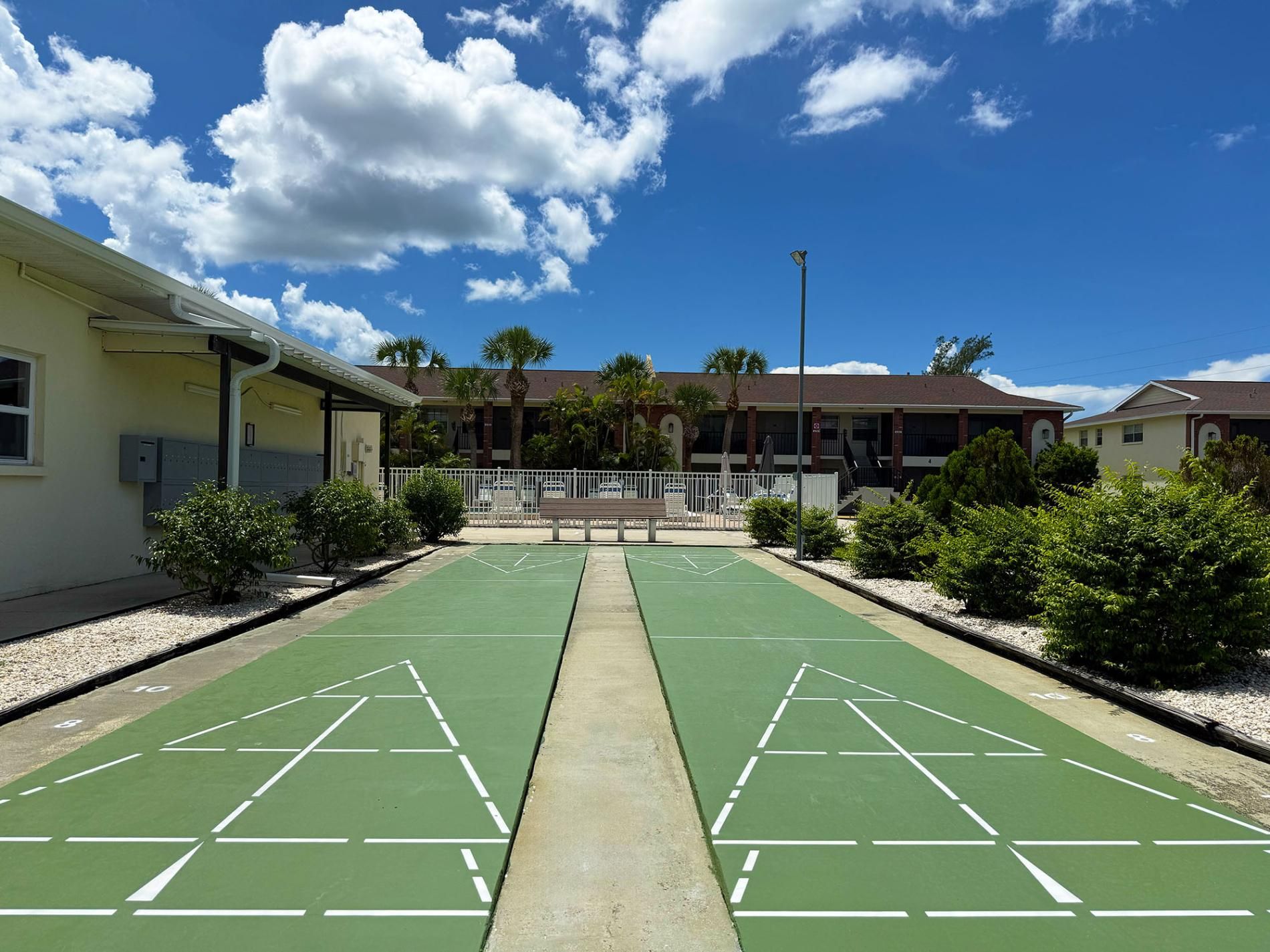 A tennis court with a net in the center, surrounded by a fence and palm trees.