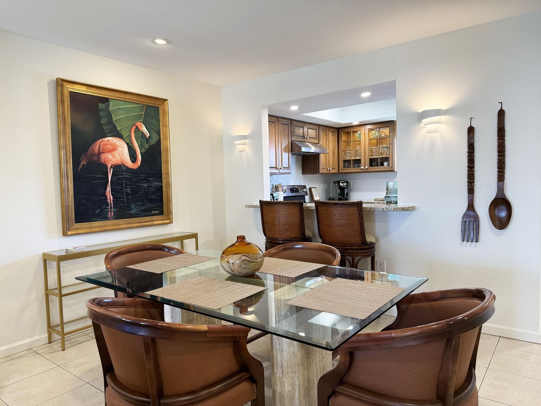 A dining area with a glass table, brown chairs, a vase, and a painting of a flamingo.