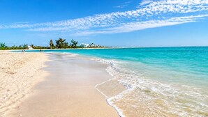A beach with clear turquoise water, a sandy shore, and a few buildings in the distance. - The Flamingo at Palm Manor – 2BR Pool View (Englewood)