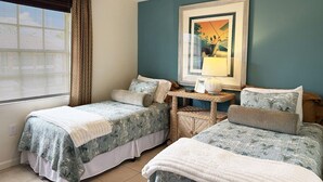 A hotel room with two beds, a small table, a chair, and a window with blinds. - The Flamingo at Palm Manor – 2BR Pool View (Englewood)