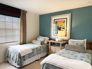 Een hotelkamer met twee bedden, een tafeltje, een stoel en een raam met zonwering.