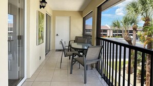 A balcony with a table and chairs, a door, and a view of palm trees and buildings. - The Flamingo at Palm Manor – 2BR Pool View (Englewood)