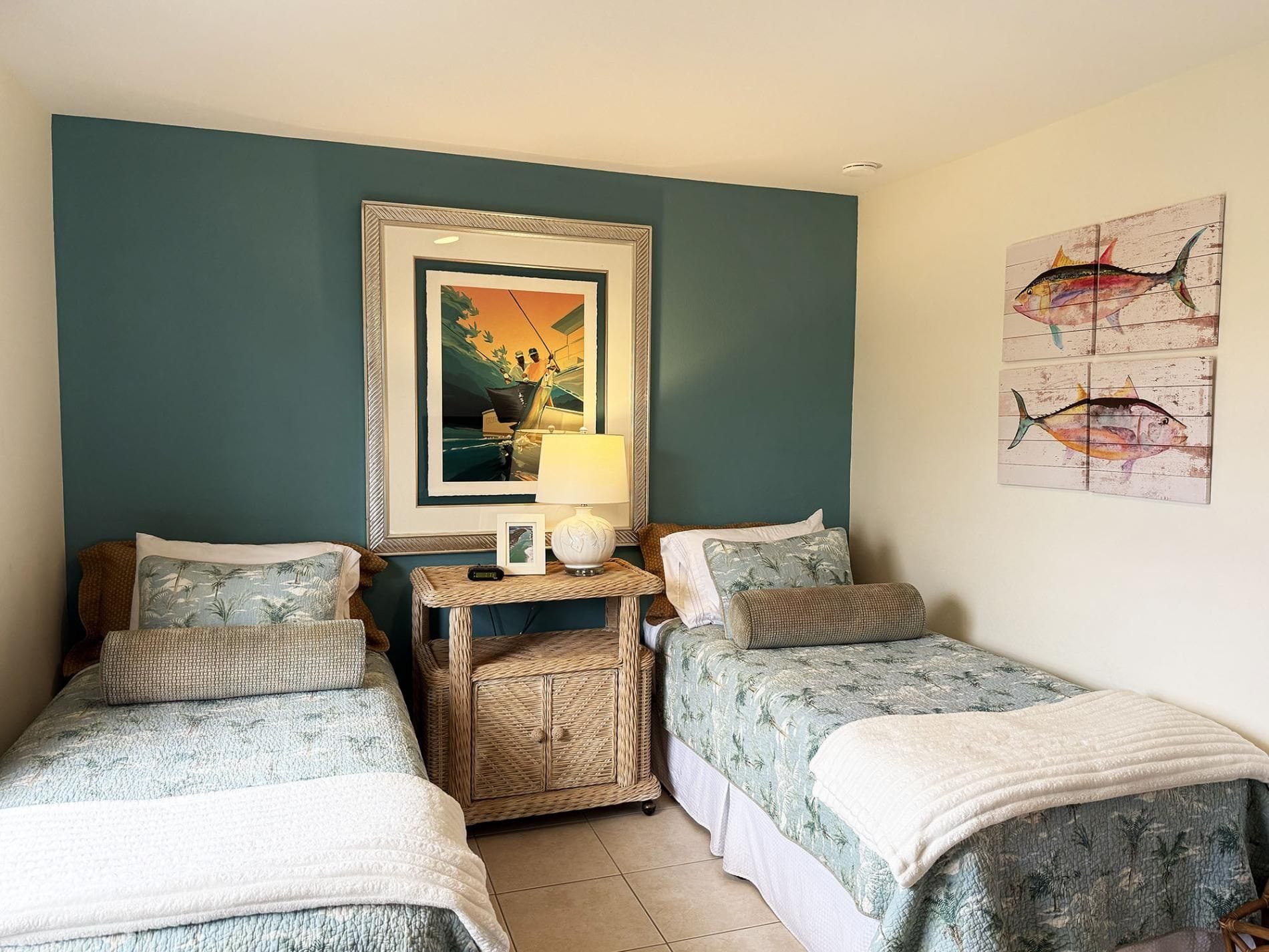 A room with two single beds, a small table with a lamp, and a framed painting above the bed.