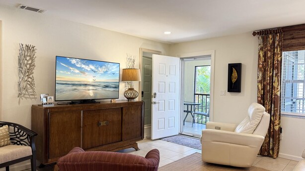 A living room with a television, a sofa, a chair, and a decorative wall piece. - The Flamingo at Palm Manor – 2BR Pool View (Englewood)