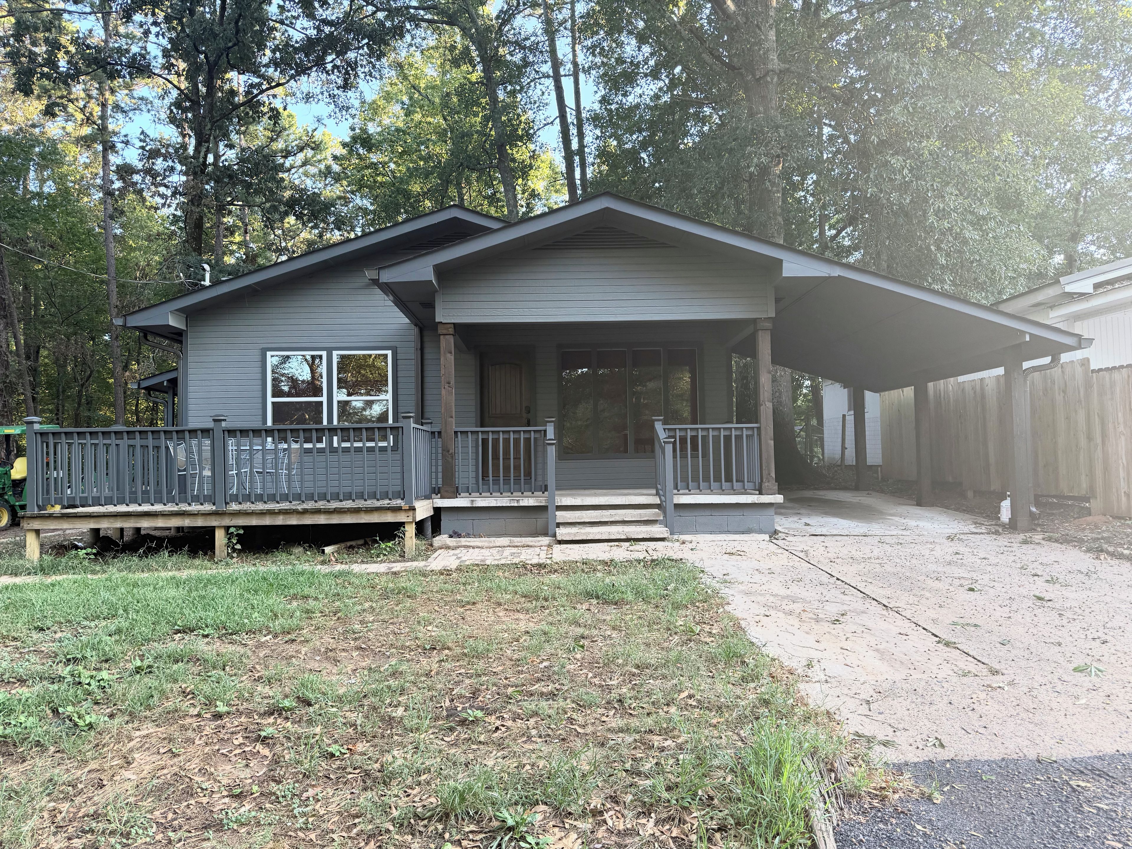 A single-story house with a porch, a fenced yard, and a dirt driveway.