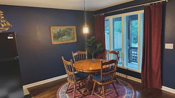 A dining area with a round table, chairs, a rug, a painting, and a window with curtains.