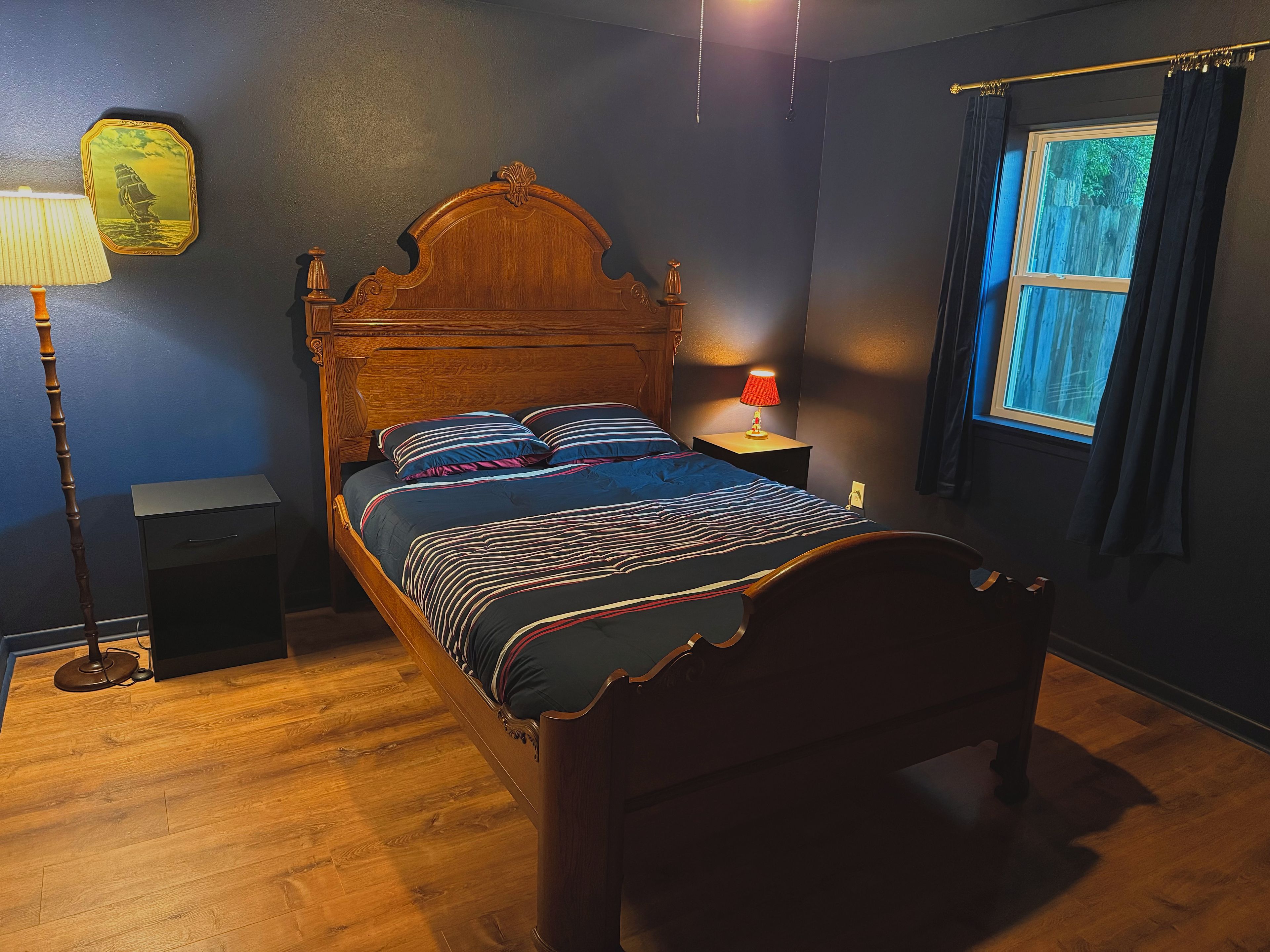 Une chambre à coucher avec un lit en bois, une table de chevet avec une lampe, une commode et une fenêtre avec des rideaux.