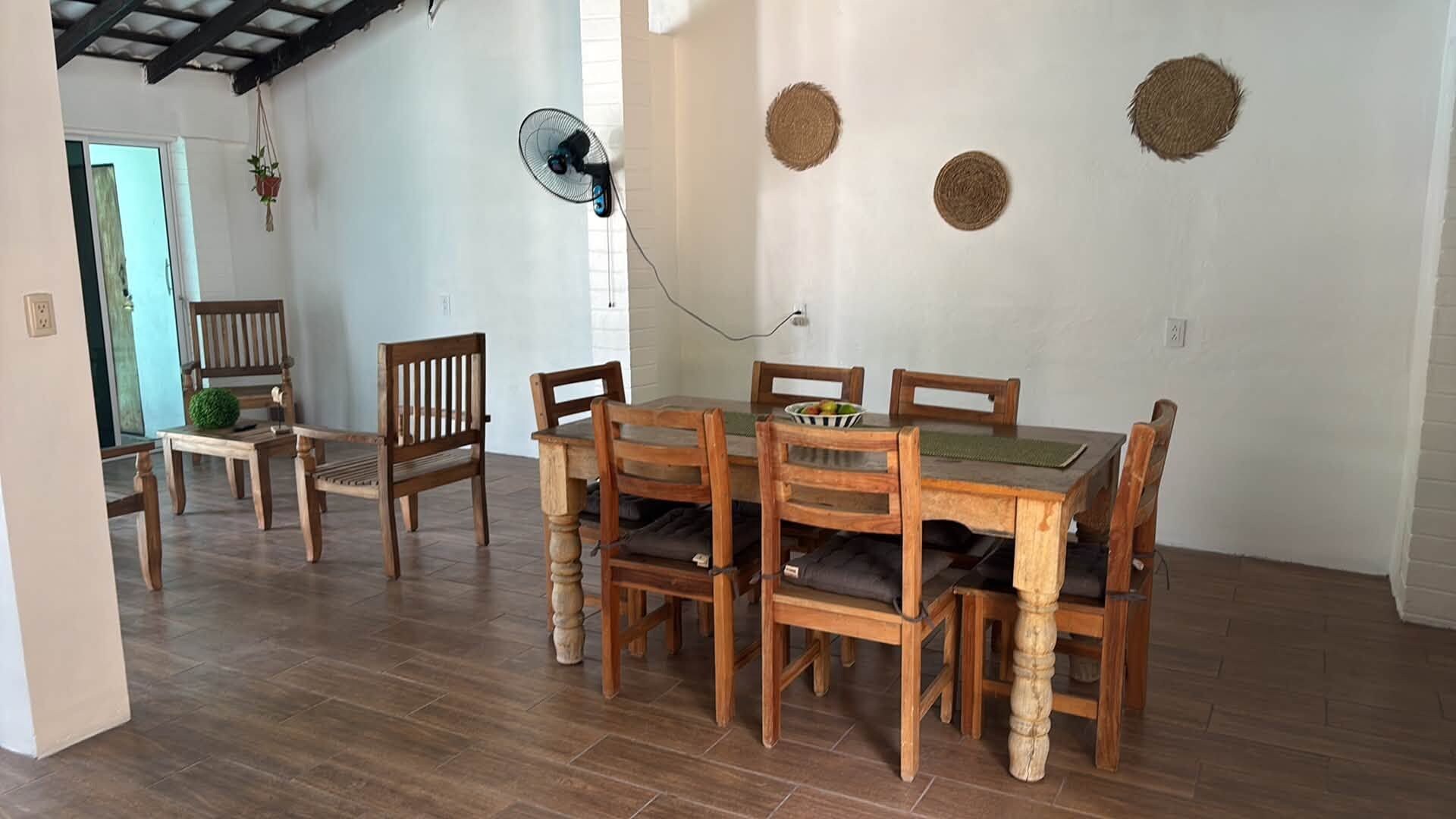 Zona pranzo con tavolo e sedie in legno, una ventola e una piccola pianta.