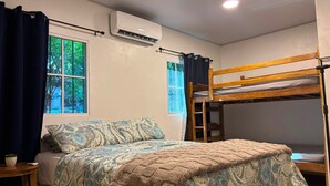 Quarto com cama beliche, janela com cortinas, ar condicionado e mesa de cabeceira com uma planta.