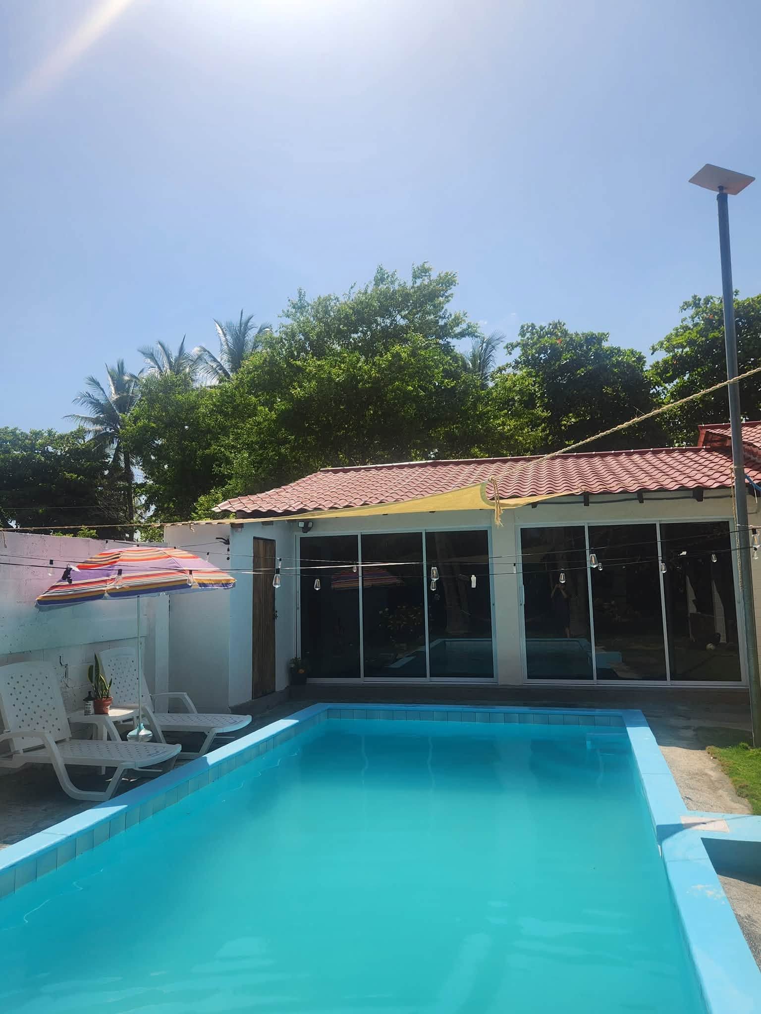 Una piscina con bordo piastrellato, una zona coperta con finestre e cielo sereno.
