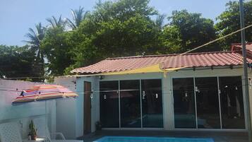 Una piscina con bordo piastrellato, una zona coperta con finestre e cielo sereno.