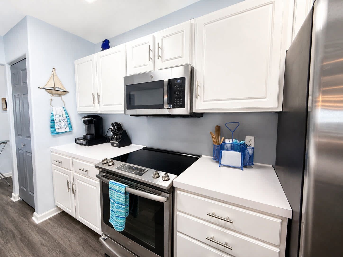 A modern kitchen with white cabinetry, a stainless steel refrigerator, a microwave, an oven, and a coffee maker.