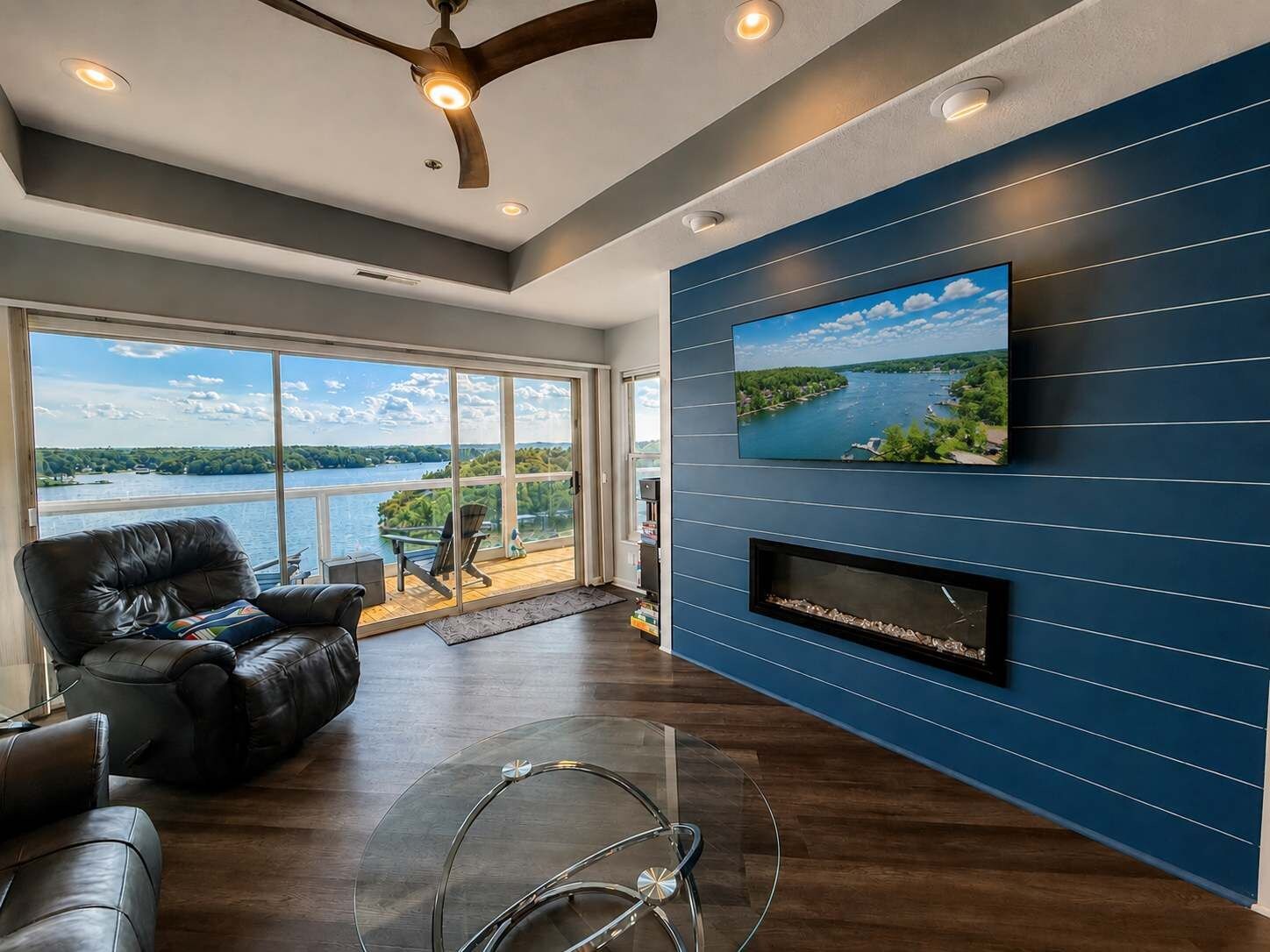 A modern living room with a large window, leather sofas, a ceiling fan, and a mounted TV.
