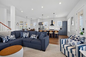 A modern living room with a sectional sofa, a round coffee table, and a patterned armchair. - Bayside Wayside - 3BR Home, Walk to Beach + Pool (Cape Charles)