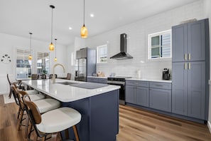 A modern kitchen with a central island, bar stools, and pendant lighting. - Bayside Wayside - 3BR Home, Walk to Beach + Pool (Cape Charles)