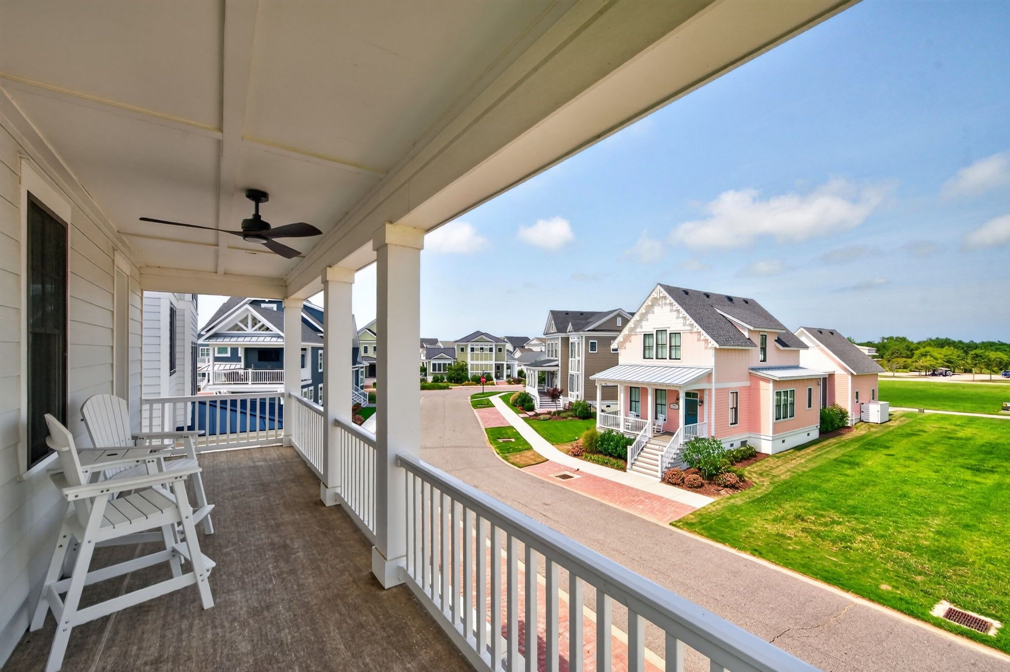 A covered porch with white rocking chairs and a view of a residential street with houses.