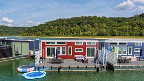 A waterfront property with multiple buildings, including a red building with a balcony and a blue building with a covered area. There are floating docks and a small inflatable pool. - Still Afloat - Floating house on Lake Cumberland (Russell Springs)