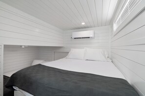 A bedroom with a bed, white walls, and an air conditioning unit mounted on the wall. - Still Afloat - Floating house on Lake Cumberland (Russell Springs)
