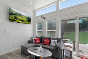 A modern living room with a grey sofa, a round table, and a TV mounted on the wall. - Still Afloat - Floating house on Lake Cumberland (Russell Springs)