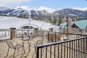 Sneeuwbedekte berglandschap met een kabelbaan, een omheind terras met buitenmeubels en een gebouw met een groen dak.