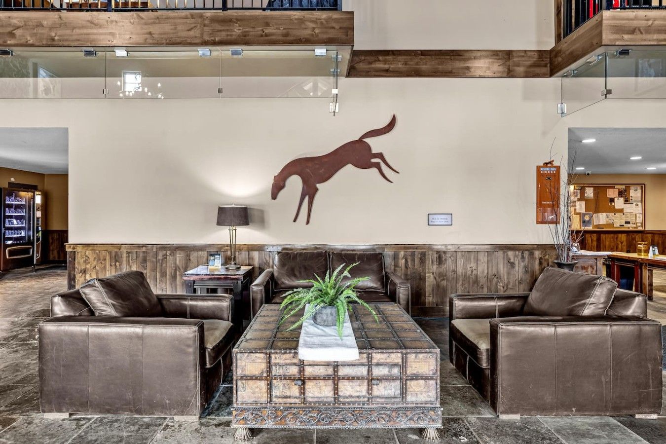 Un hall d’entrée avec des canapés en cuir, une table basse en bois et une silhouette de cheval fixée au mur.