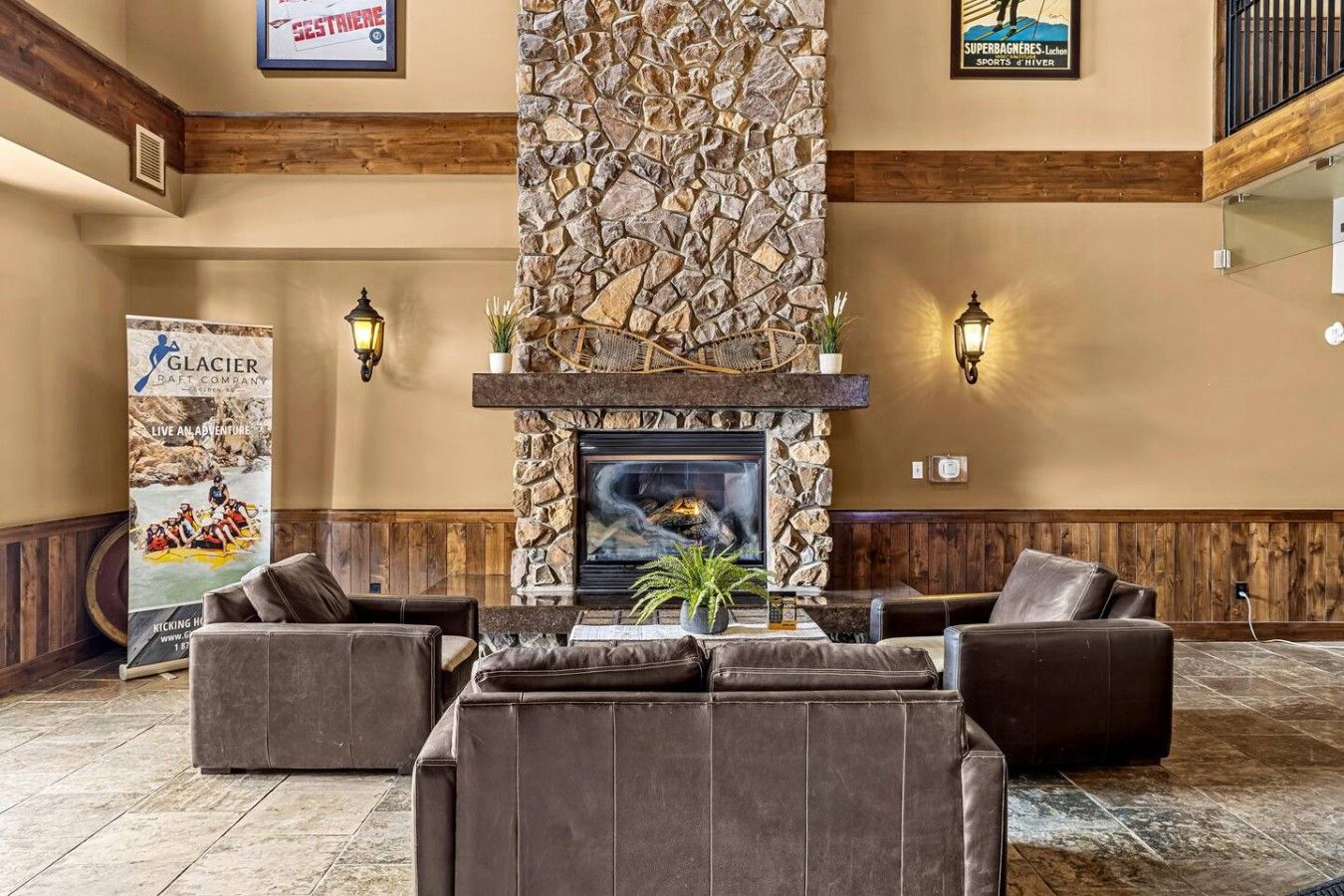 A lobby with a stone fireplace, leather sofas, and a banner for Glacier Raft Company.