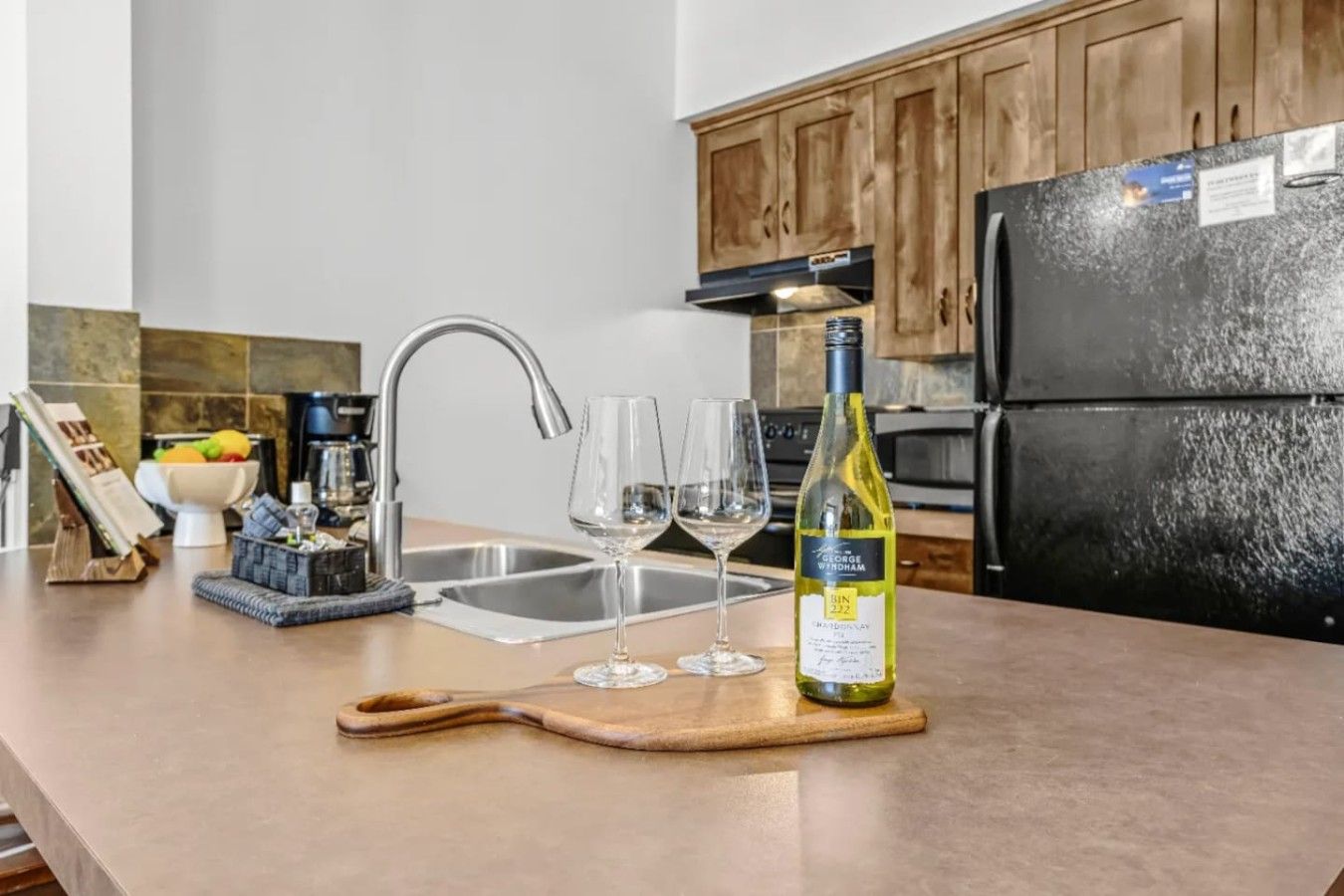 A kitchen counter with a wine bottle, two wine glasses, and a cutting board.