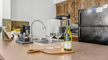 A kitchen counter with a wine bottle, two wine glasses, and a cutting board.