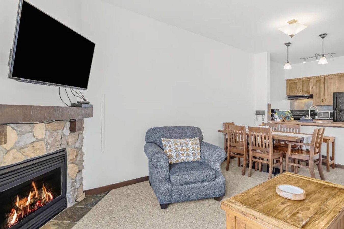 A living room with a fireplace, a television mounted on the wall, and a dining area with wooden furniture.