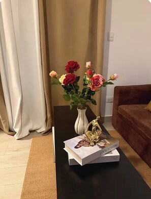 Un salon avec une table basse noire, un vase de fleurs, un livre et un canapé marron.