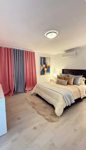 Une chambre à coucher avec un lit, des rideaux, un tableau, une table de chevet et un luminaire au plafond.