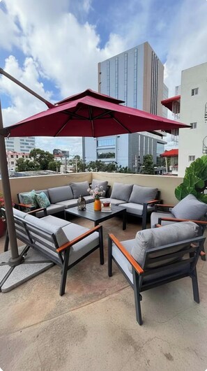 An outdoor seating area with a red umbrella, grey sofas, and a coffee table. - Your beautiful, cozy, and very centrally located apartment (Santo Domingo)
