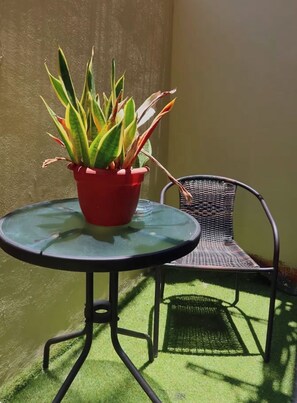 Une petite table ronde, agrémentée d’un pot de fleurs et d’une chaise en osier, dans un espace extérieur baigné de soleil.