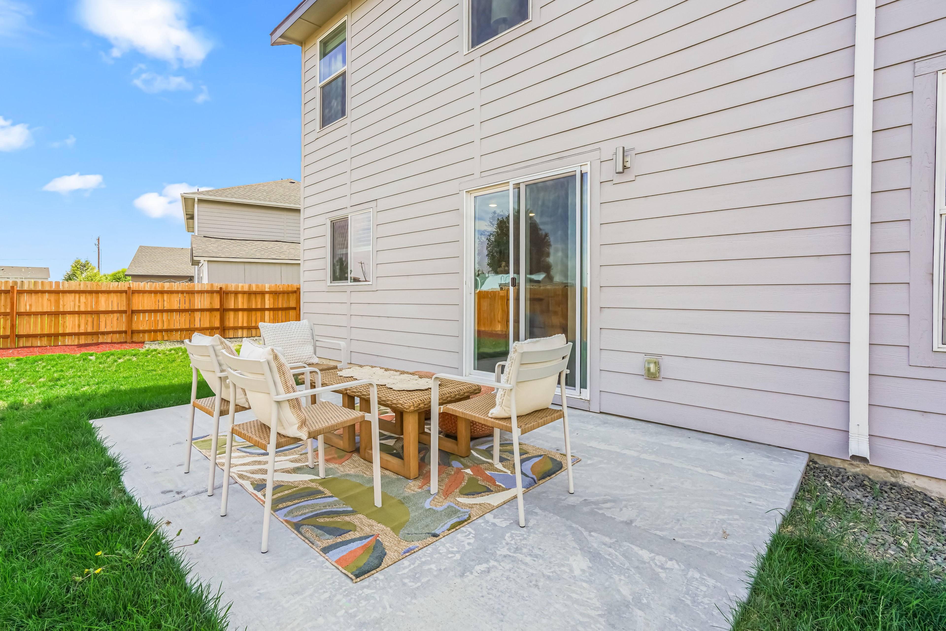 Un patio con una mesa, sillas, una valla de madera y un césped.