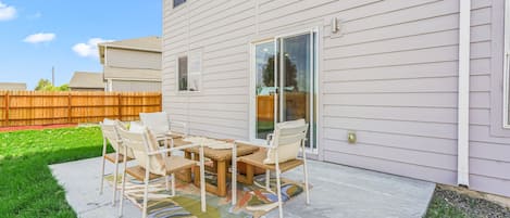 Un patio con una mesa, sillas, una valla de madera y un césped.