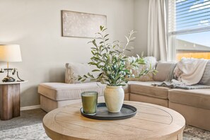 Un salon avec une table basse ronde en bois, une plante en pot et un verre d’une boisson verte.